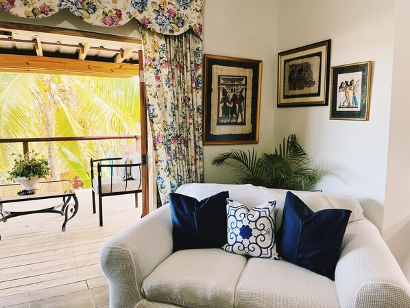 A living room with a sofa, a table, chairs, and a view of palm trees through a window.