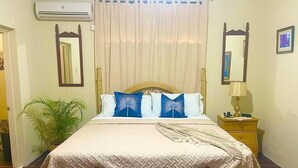 A neatly made bed with a wooden headboard, a bedside table with a lamp, and a potted plant.