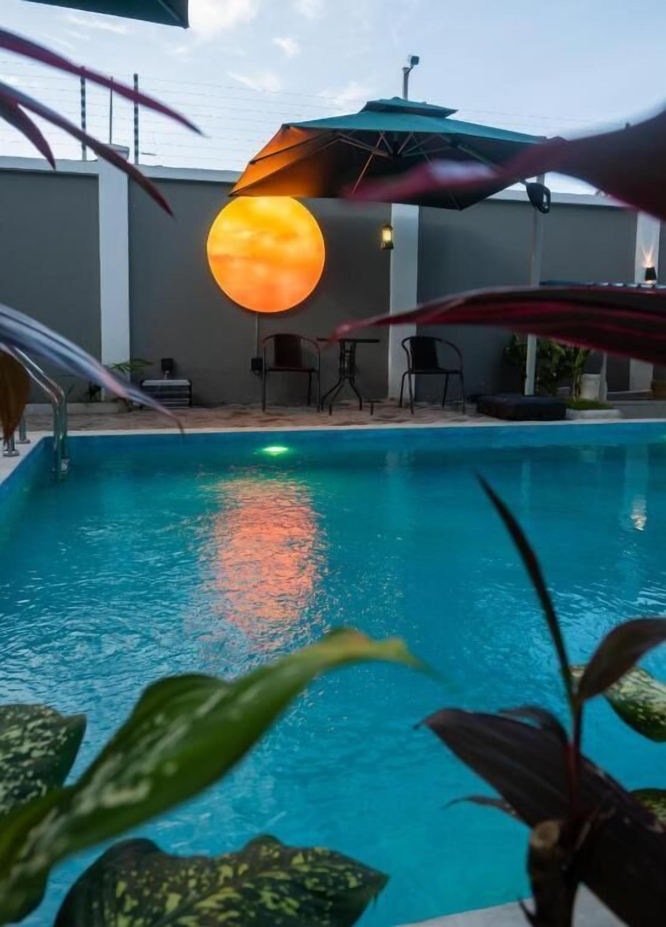 Piscina com vista para o pôr do sol, rodeada por cadeiras e uma mesa.