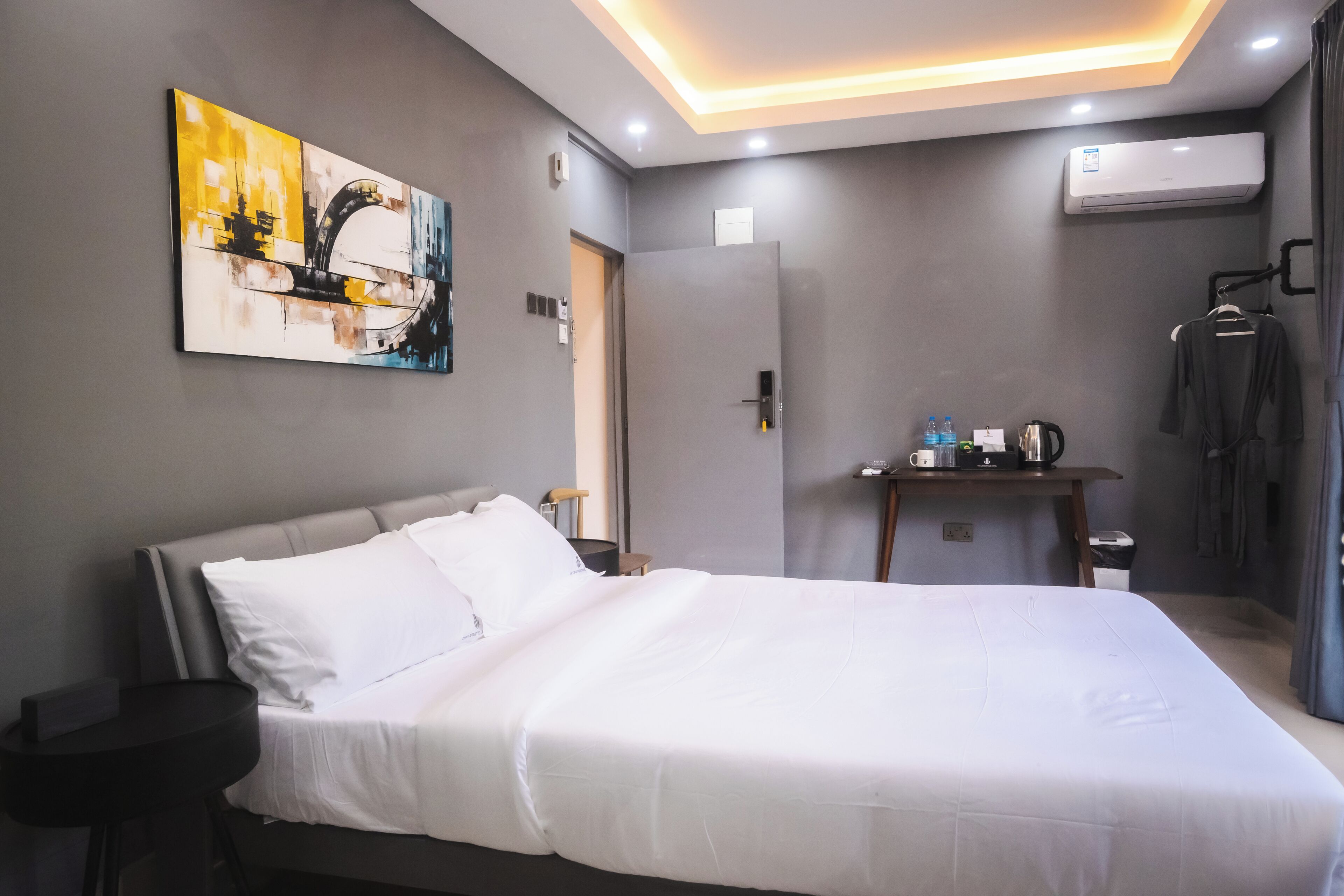 Habitación de hotel con cama, un cuadro en la pared, aire acondicionado, escritorio con hervidor y armario.