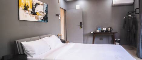 Habitación de hotel con cama, un cuadro en la pared, aire acondicionado, escritorio con hervidor y armario.