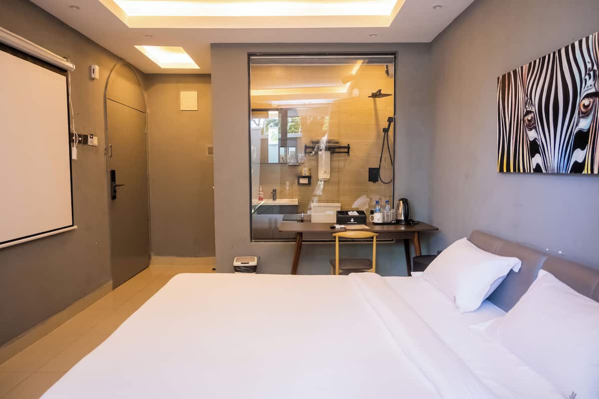 Ein Hotelzimmer mit einem großen Bett, einem Schreibtisch mit Stuhl, einem Spiegel und einem Duschbereich.