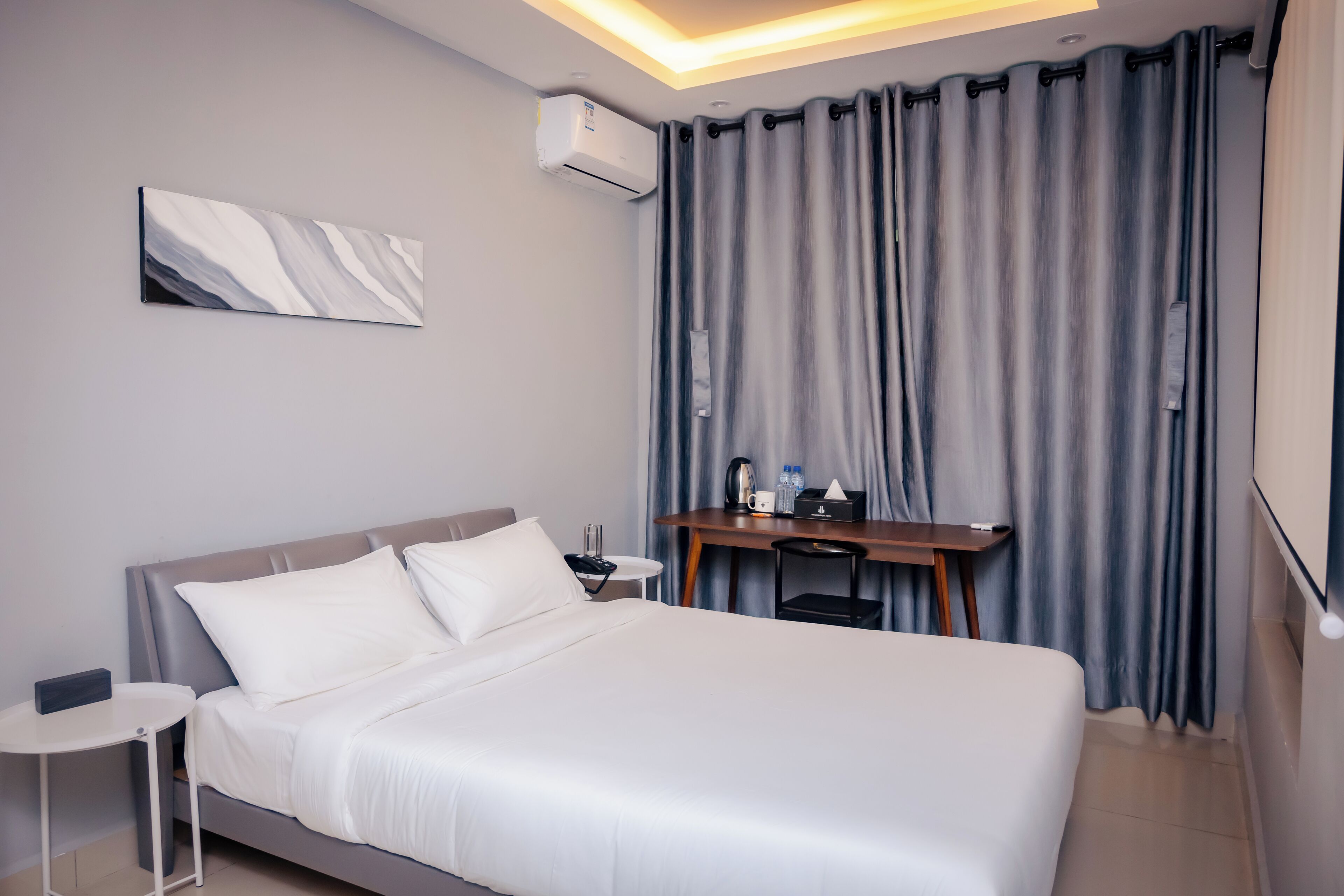 A hotel room with a bed, bedside table, desk, and curtains.