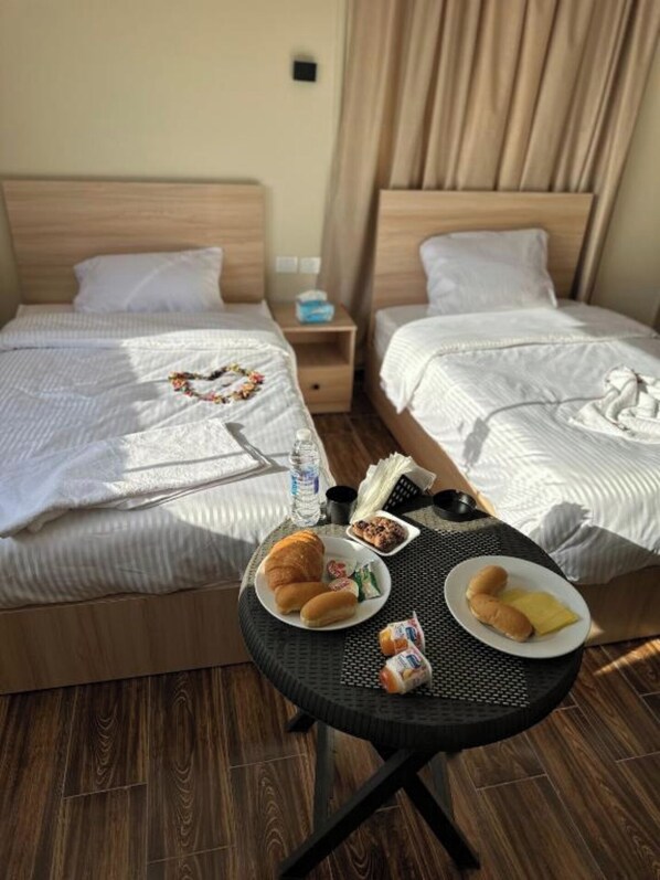 Two single beds with white comforters and pillows, a nightstand, and a round table with breakfast essentials.