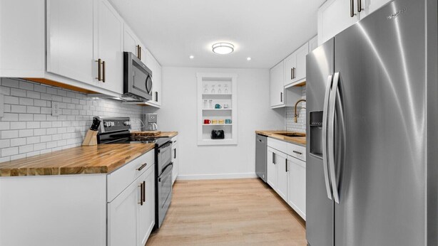 A modern kitchen with white cabinetry, stainless steel appliances, and a wooden countertop.