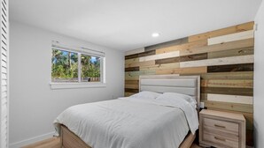 A bedroom with a bed, a nightstand, a window, and a wooden wall panel.