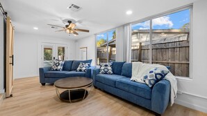 A spacious living room with a large window, a ceiling fan, and a wooden floor.