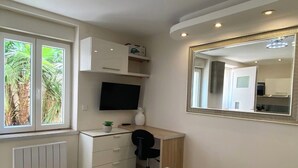 Une chambre à coucher comprenant un lit, un bureau avec une chaise, une télévision, un miroir et une fenêtre donnant sur un paysage verdoyant.