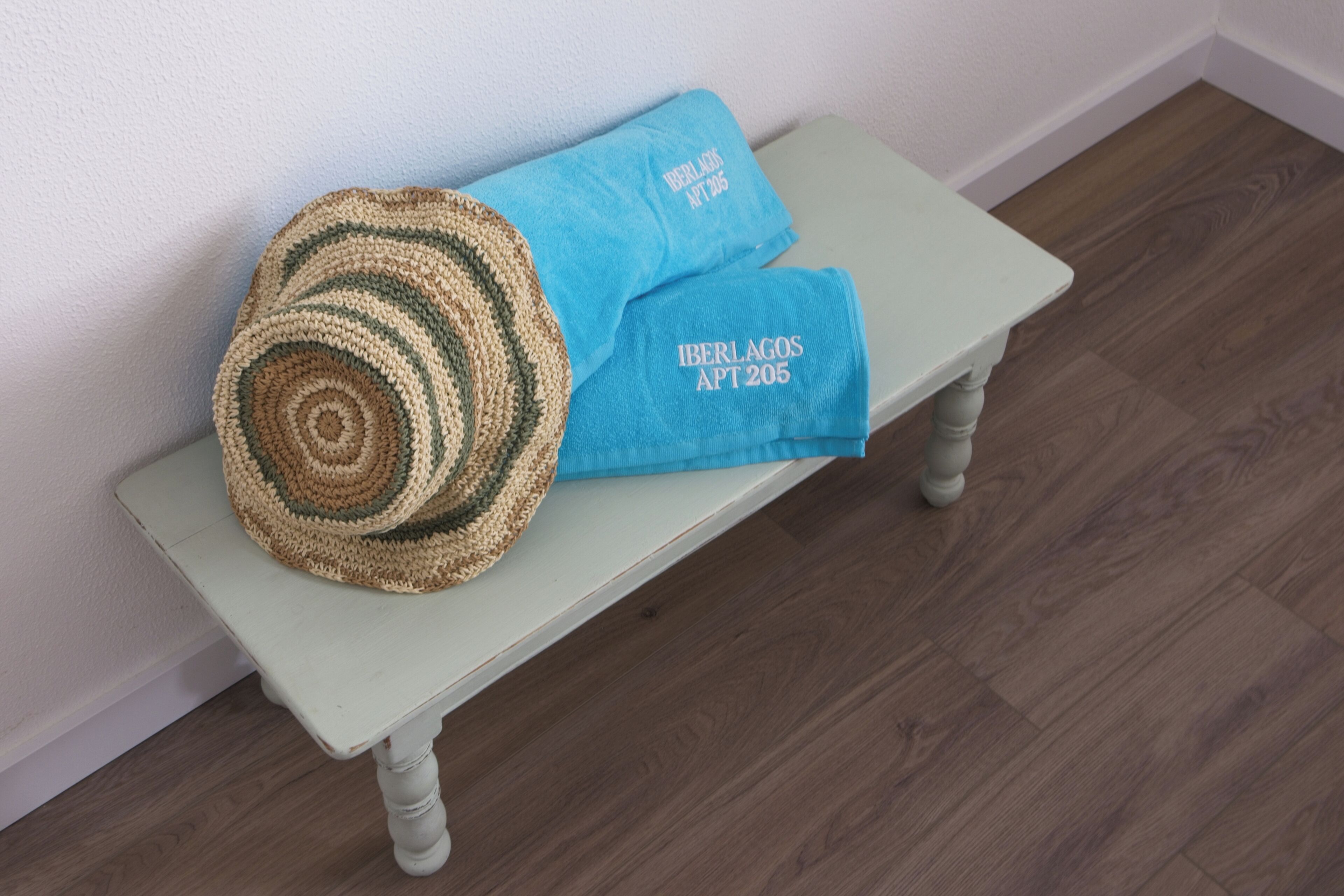 A light blue bench with a crocheted pillow and a matching blue towel with embroidered text.