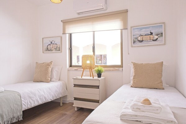Une chambre avec deux lits, une fenêtre donnant sur un beau paysage, une table de chevet avec une lampe et des œuvres d’art accrochées aux murs.