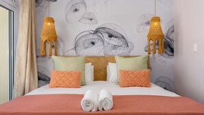 Een net opgemaakt bed met een rode deken, twee oranje kussens en een paar opgerolde handdoeken.