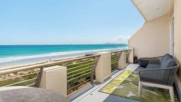 Een balkon met uitzicht op het strand, een bank en een kamerbreed tapijt met dessin.