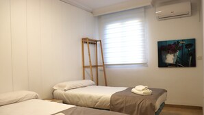 A hotel room with two beds, a window with blinds, an air conditioner, and a painting on the wall. - Apartment for groups with free parking  (Sevilla)
