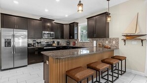 A modern kitchen with dark wood cabinets, stainless steel appliances, a granite island with bar stools, and a sailboat decoration on the wall. - EV_9026 - 6 Bed 6 Bath Home with Screened-In Private Pool with Spillover Spa and (Davenport)