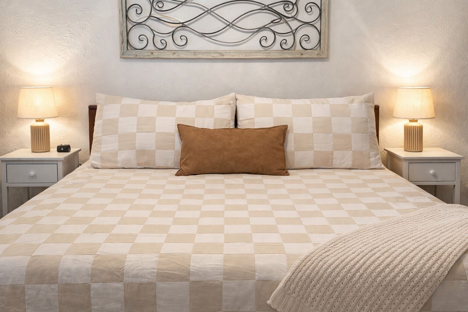 A neatly made bed with a checkered bedspread, two pillows, and a blanket. There are two bedside tables with lamps and a decorative wall piece above the bed.