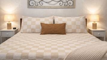 A neatly made bed with a checkered bedspread, two pillows, and a blanket. There are two bedside tables with lamps and a decorative wall piece above the bed.
