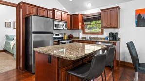 A modern kitchen with wooden cabinets, stainless steel appliances, granite countertops, and a bar area with two chairs.