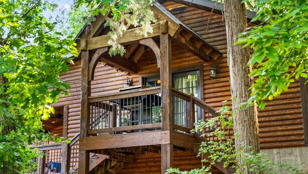 A rustic log cabin with a balcony and a staircase leading to the entrance.