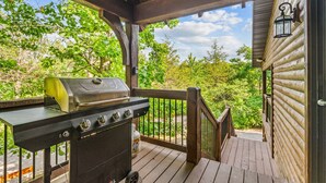 A covered deck with a grill and a lantern, overlooking a wooded area.