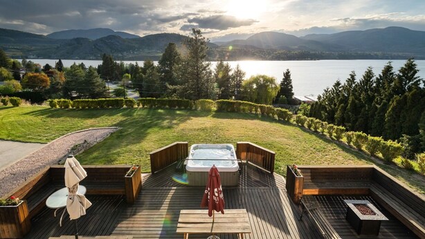 Une terrasse en bois avec un jacuzzi, un coin salon et une vue sur un lac et des montagnes.