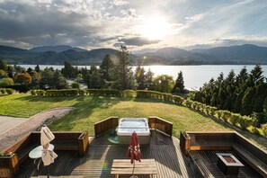 A wooden deck with a hot tub, seating area, and a view of a lake and mountains.