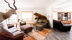 Un salon avec un canapé, un pouf et une statue d’ours posée sur une chaise.