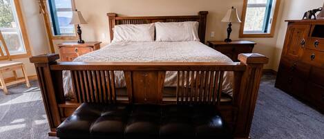 A wooden bed with a bench in front, two bedside tables, and a dresser.