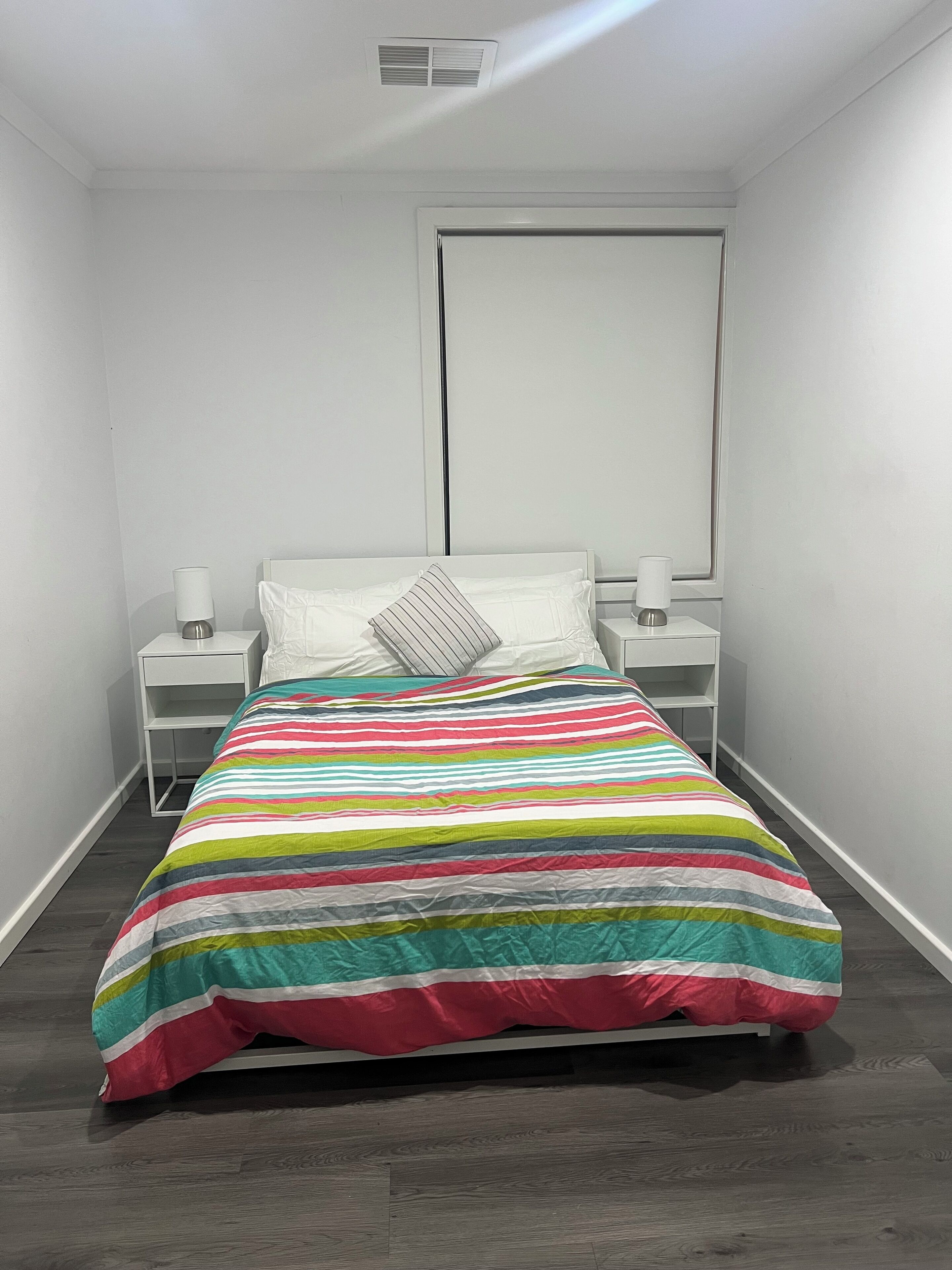Ein kleines, modernes Schlafzimmer mit einem Einzelbett, weißen Nachttischen und einem Fenster.