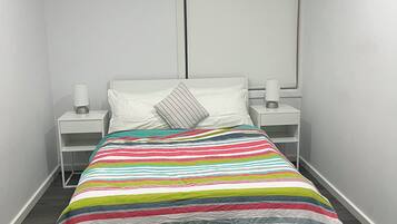 Ein kleines, modernes Schlafzimmer mit einem Einzelbett, weißen Nachttischen und einem Fenster.
