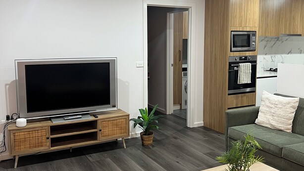 Un soggiorno moderno con una TV a schermo piatto, un mobile TV in legno, un divano verde, un tavolino da caffè in legno e una pianta in vaso.