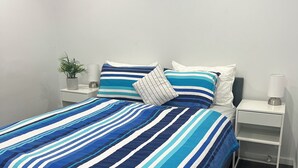 Un letto rifatto con cura, con una coperta a righe blu e bianche, un vaso di piante e un comodino con una lampada.