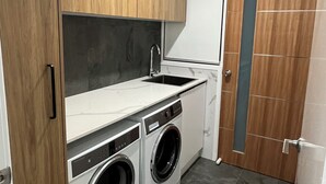 Una lavanderia piccola e funzionale, con pensili in legno, una lavatrice e un lavandino.