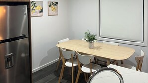 Una cucina moderna con un frigorifero in acciaio inossidabile, un tavolo da pranzo in legno con sedie, un lavello con piano di lavoro in marmo e una finestra con persiane.