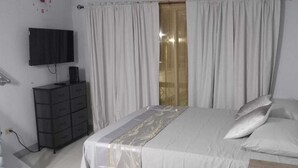A bedroom with a bed, white curtains, a TV, and a dresser. - Cozy Studio with Loft WiFi and AC in New Kingston (Kingston)