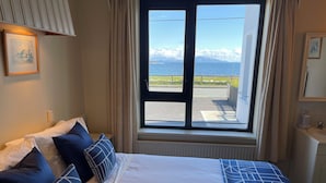 A bedroom with a bed, pillows, a window with a view of mountains and a body of water, and a radiator. - Spacious 5-bedroom house with sea views for up to 12 guests in beautiful Achill (Dooagh, Achill Island)
