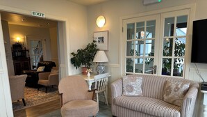 A living room with a striped sofa, a white armchair, a small table, and a potted plant. There is a window with multiple panes and a door labeled "EXIT". - Spacious 5-bedroom house with sea views for up to 12 guests in beautiful Achill (Dooagh, Achill Island)
