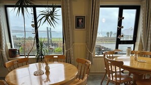 A dining area with a round wooden table and chairs, a vase with flowers, and a view of the sea through large windows. - Spacious 5-bedroom house with sea views for up to 12 guests in beautiful Achill (Dooagh, Achill Island)