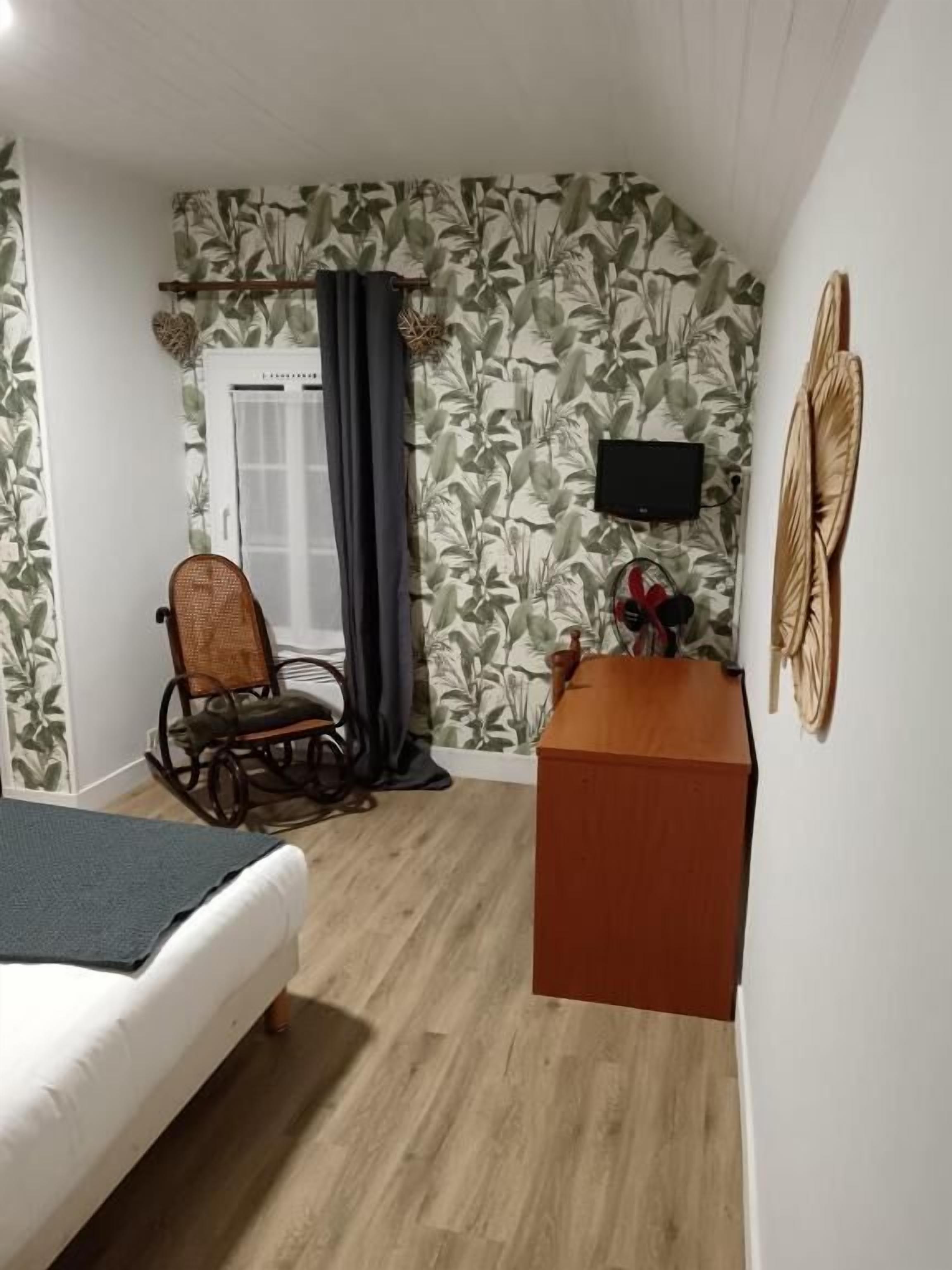 A room with a bed, a rocking chair, a desk, a television, and a wall with a leaf pattern.
