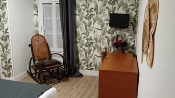 A room with a bed, a rocking chair, a desk, a television, and a wall with a leaf pattern.