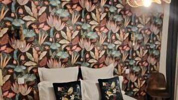 Un letto con lenzuola bianche e una coperta scura, una parete con motivo floreale e un lampadario.