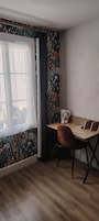 A room with a wooden desk, a chair, a window with curtains, and a patterned wall.