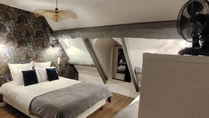 Una camera da letto con un letto, cuscini, un ventilatore e una parete decorata con un motivo a foglia.