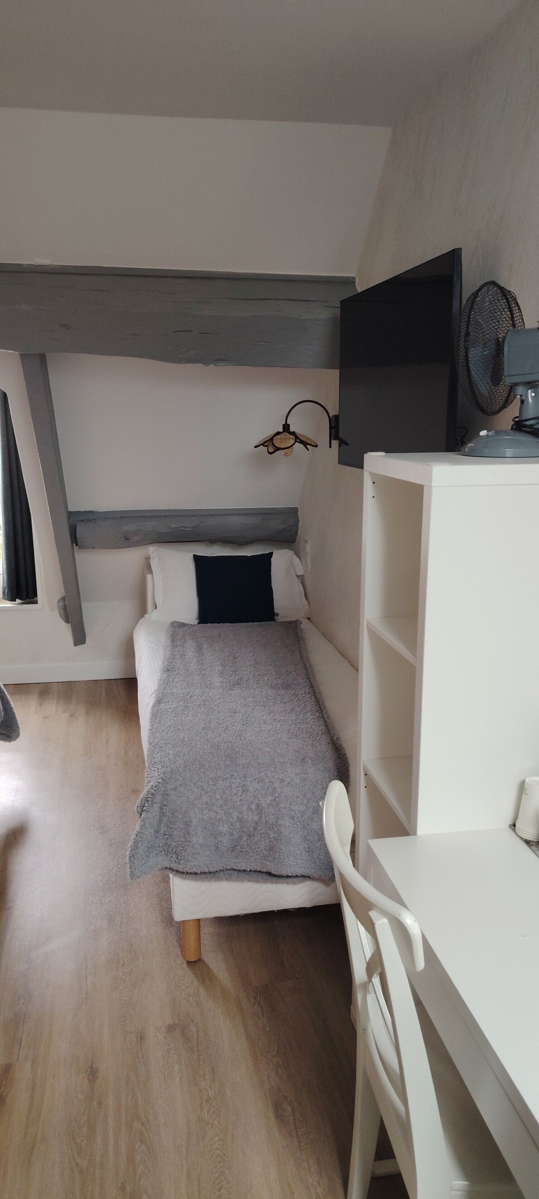 Een kleine, netjes ingerichte slaapkamer met een bed, een bureau en een stoel.