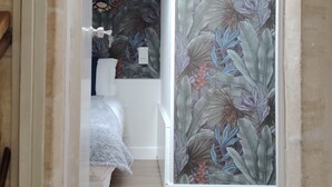 Un corridoio stretto che conduce a una camera da letto con un letto, una finestra e una parete decorata con un motivo a foglia tropicale.