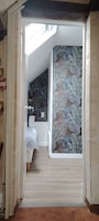 A narrow hallway leading to a bedroom with a bed, a window, and a wall with a tropical leaf pattern.