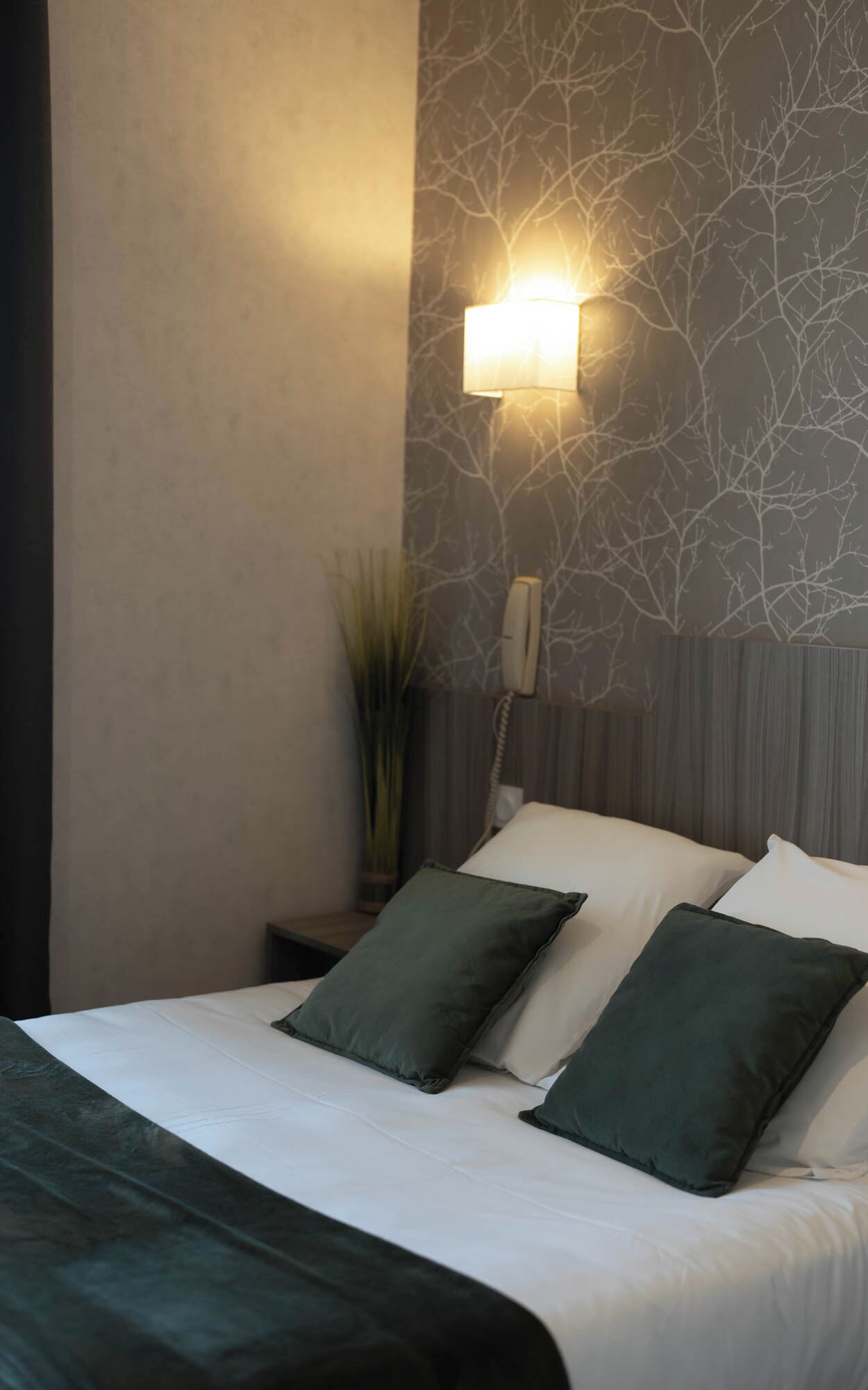A neatly made bed with two pillows, a bedside phone, and a wall-mounted light fixture.