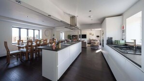 Une cuisine spacieuse dotée d’un îlot central, d’un coin repas avec des chaises en bois et d’une grande fenêtre qui laisse entrer la lumière naturelle.