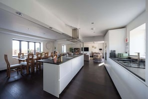 A spacious kitchen with a central island, dining area with wooden chairs, and a large window providing natural light.