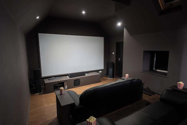 A home theater with a large screen, black leather seating, popcorn, and a dark interior.