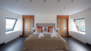 Une chambre spacieuse avec un grand lit, deux fenêtres et une vue sur l’extérieur.